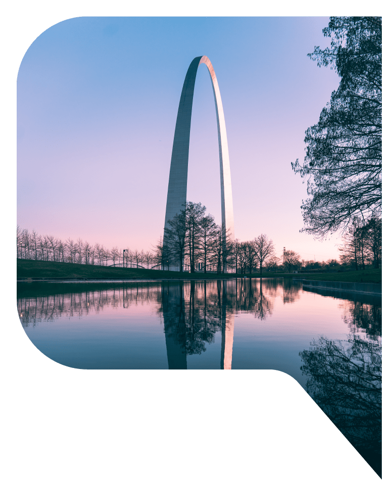 A view of the Gateway to the West arch in Saint Louis, Missouri, reflected in a man-made pond at sunset.
