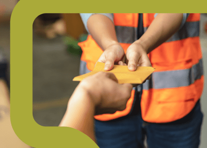 Close up on the hands of a warehouse worker handing an envelope to another person.