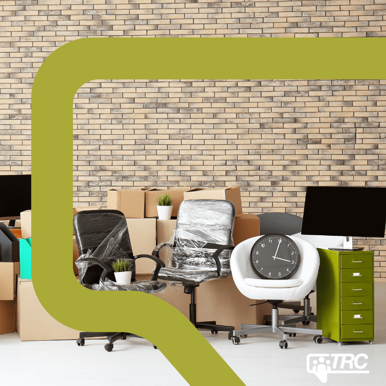 A large room with office equipment and unpacked boxes in front of a brick wall.