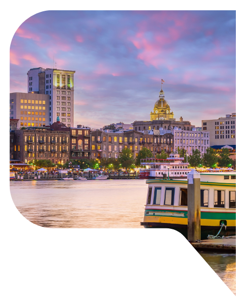Sunset view of Savannah, Georgia with the river and a small ferry in the foreground.