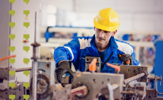 Factory worker in blue coveralls and a yellow hard hat operating a metal machine in a workshop with safety gear on
