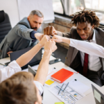 Team of coworkers in a meeting high-fiving around a conference table, celebrating collaboration