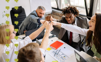 Team of coworkers in a meeting high-fiving around a conference table, celebrating collaboration