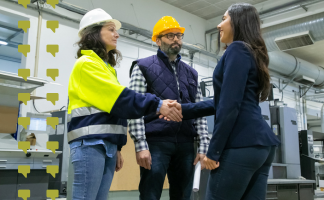 Two women and a man in safety gear shake hands in an industrial facility, signaling a meeting or agreement.