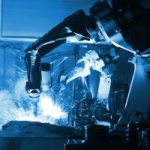Industrial robotic arms welding metal parts on a production line with bright sparks flying.